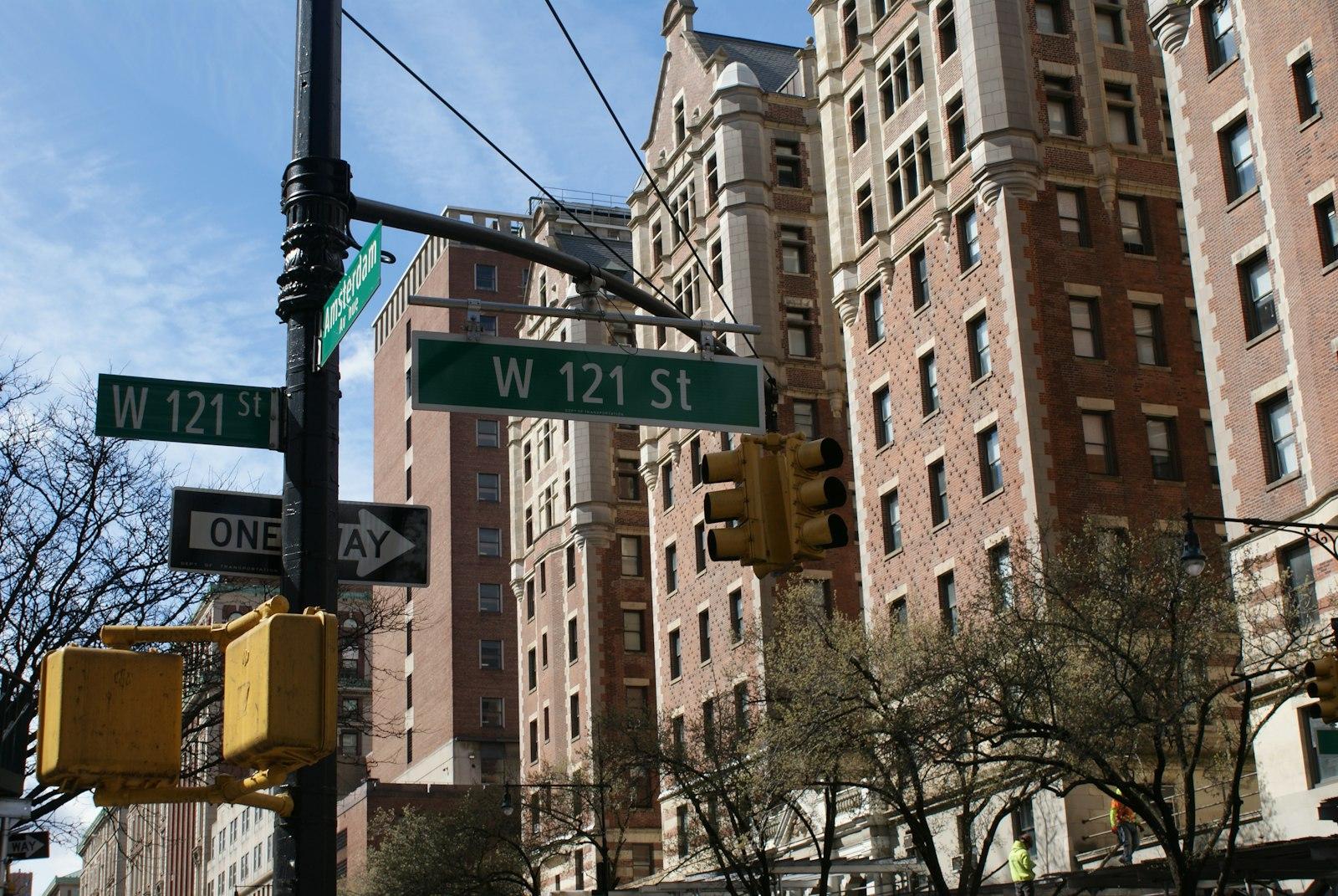 Urban street scene showing a red traffic signal and directional street signs mounted on poles against a city backdrop