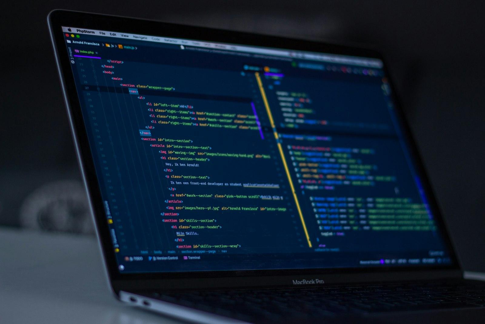 Over-the-shoulder view of a MacBook Pro screen showing a code editor with colorful syntax-highlighted source code