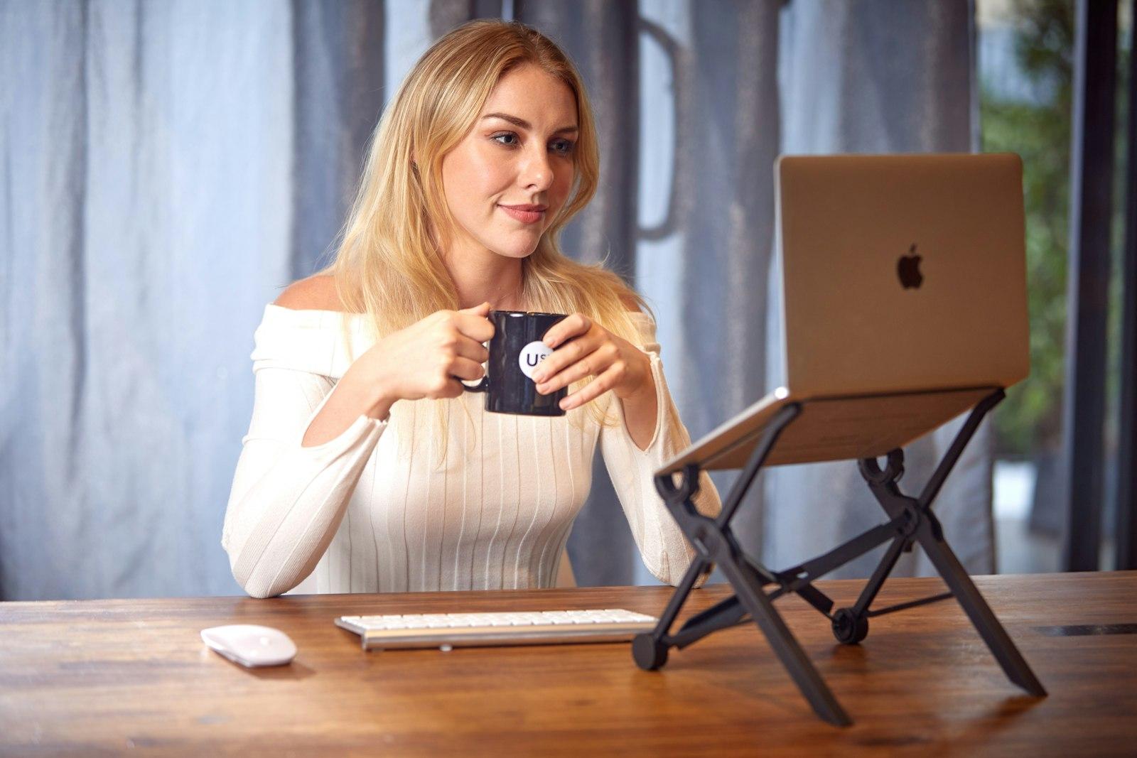 A woman working on a laptop at a table with a cup of coffee nearby