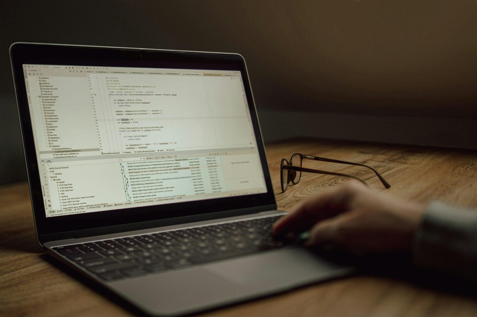 Developer's hands typing on a laptop keyboard with glowing green code displayed on the monitor screen